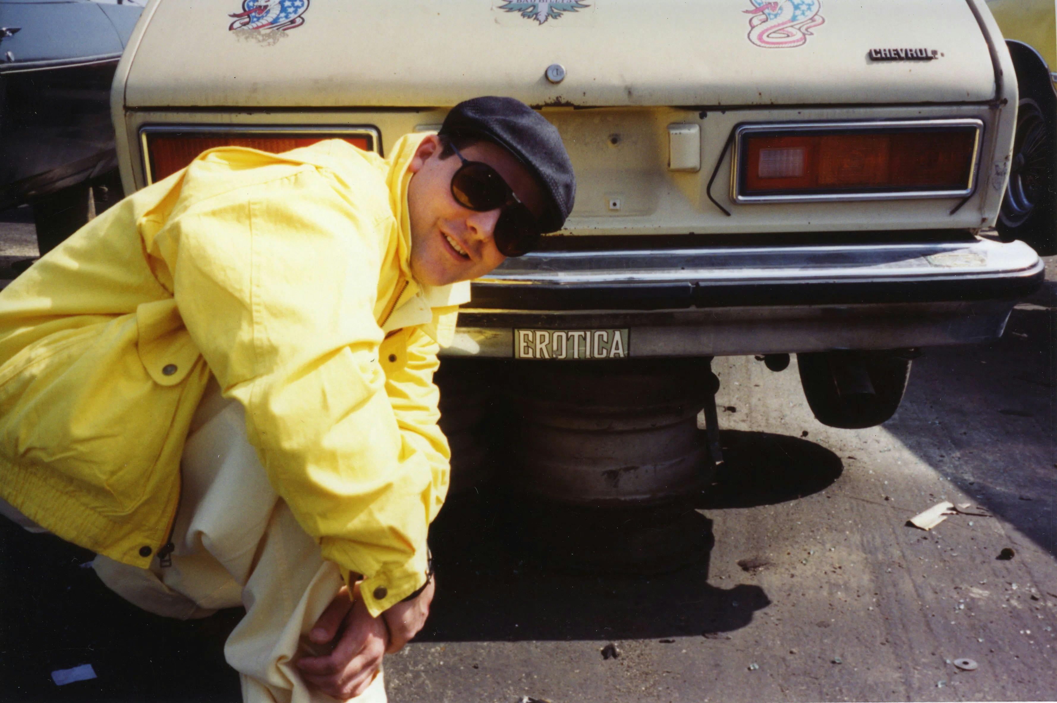 A photo of Jason Rhoades kneeling in front of a car, dated 1994