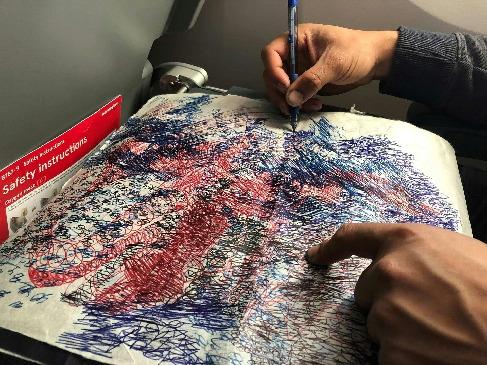 A photograph of Oscar Murillo drawing during a plane journey, dated 2019.