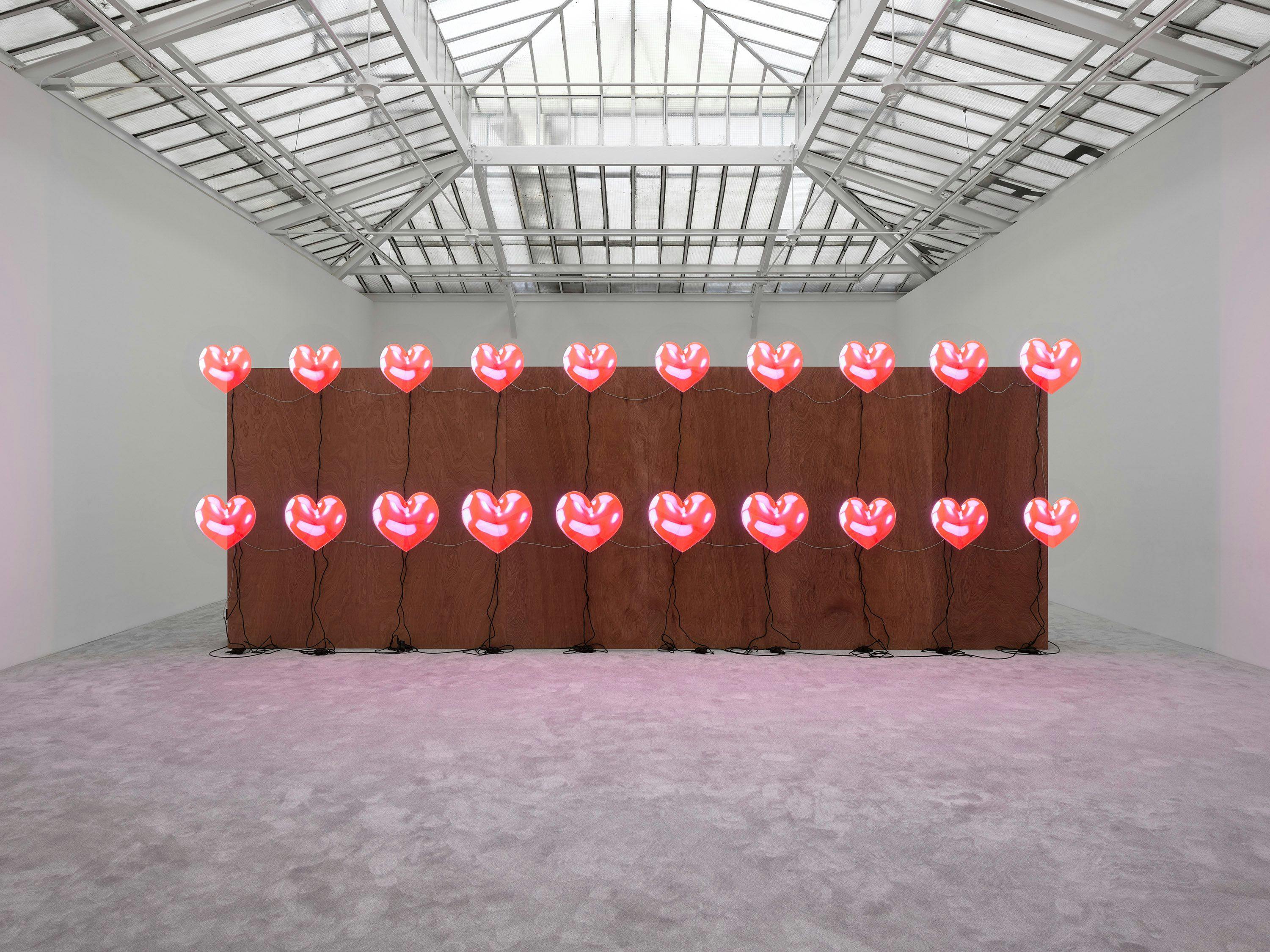 Twenty holographic displays mounted on freestanding plywood wall with mixed media by Jordan Wolfson, titled ARTISTS FRIENDS RACISTS, 2019 to 2020.